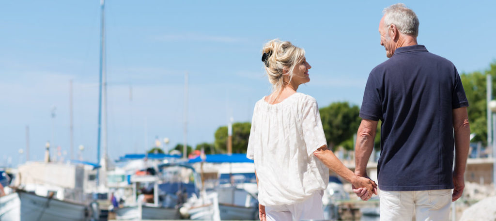 A man and woman walking hand in hand along the marina smiling at each other signifying a healthy sex life.